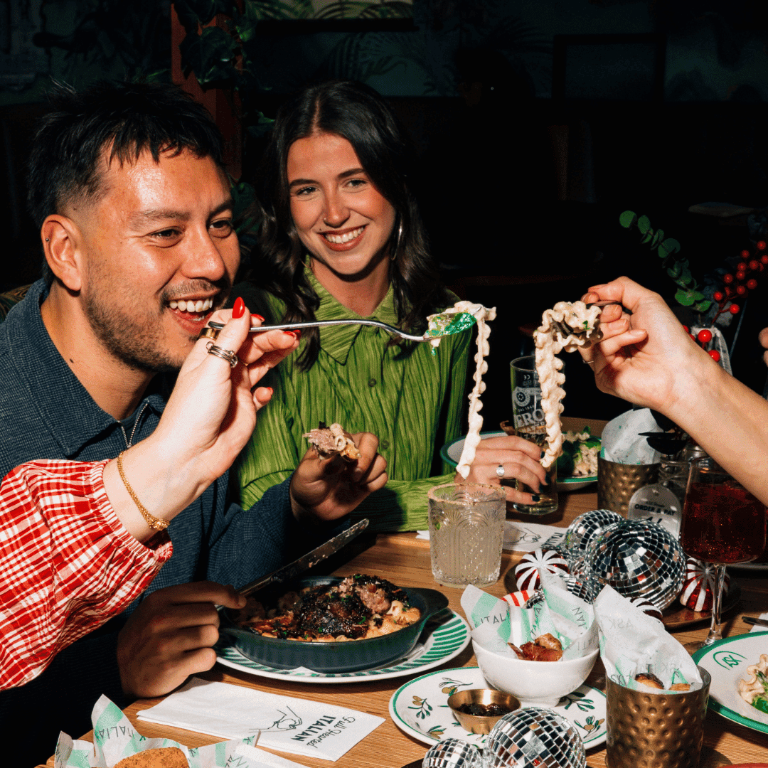 A group of people enjoying a Christmas lunch at ASK Italian restaurants, with two people and two forks of pasta being lifted up.